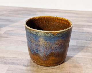A small ceramic cup with cascading glazes around the outside.