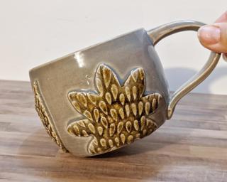 A lovely round ceramic mug with textured flowers and leaves around the outside.