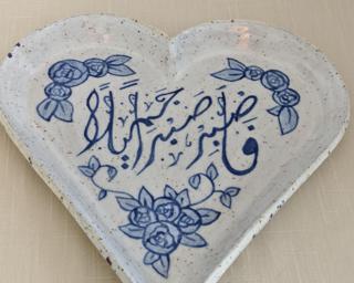 A pretty handmade heart-shaped dish decorated with Arabic calligraphy and flowers in a beautiful delft blue glaze.