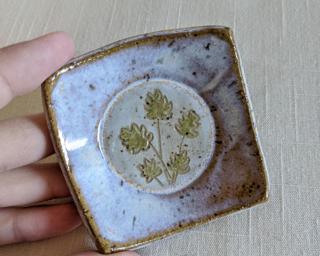 A little handmade square dish decorated with a sprig of leaves which have been carefully carved for added detail.