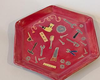 A handmade serving platter decorated with a variety of colorful tools which have been carefully carved for added detail.