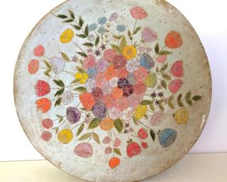 A large handmade dish hand painted with various colorful flowers which have been carefully carved for added detail.