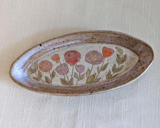 A handmade oblong-shaped dish decorated with various colorful flowers which have been carefully carved for added detail.