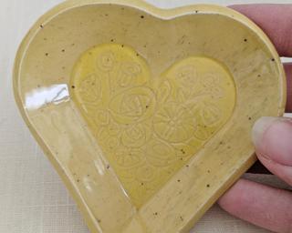 A small handmade heart-shaped dish decorated with a various hand drawn flowers.