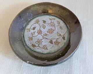 A handmade saucer decorated with vines and colorful flowers which have been carefully carved for added detail.