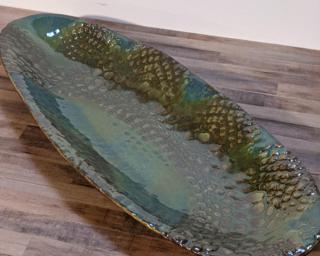 An oval shaped dish with green and blue colors over a lace pattern. Colors are slightly off