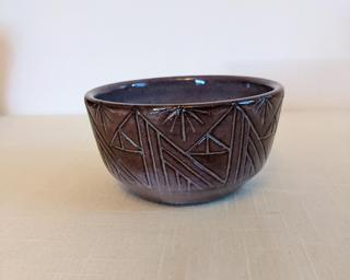 A small handle-less ceramic cup with a subtle purple glaze over a mid-fire dark brown clay.