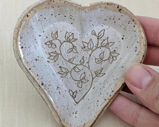 A small handmade heart-shaped dish decorated with a sweet little leafy vine.