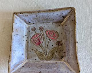 A little handmade square dish decorated with a variety of colorful flowers which have been carefully carved for added detail.