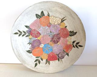 A large handmade dish decorated with various colorful flowers which have been carefully carved for added detail.