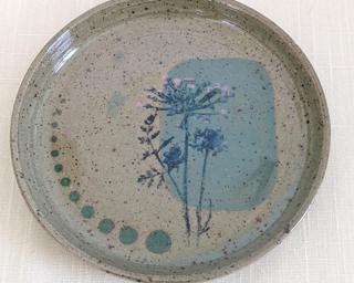 A small wheel thrown dish decorated with stamped flowers on a brown speckled clay body.