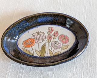 A small handmade oblong-shaped dish decorated with various colorful flowers which have been carefully carved for added detail.