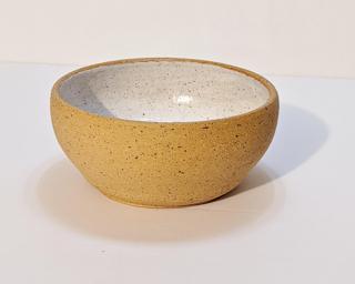 A small handle-less ceramic cup with a white glaze over a mid-fire speckled clay.